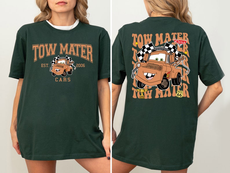 K&ouml;nnte beinhalten: Gr&uuml;nes T-Shirt mit einem braunen Cartoon-Abschleppwagen auf der Vorderseite und dem Text "Tow Mater Est. 2006 Cars". Die R&uuml;ckseite des Shirts hat den Text "Tow Mater" in einem wellenf&ouml;rmigen Muster wiederholt, mit einem braunen Cartoon-Abschleppwagen in der Mitte.