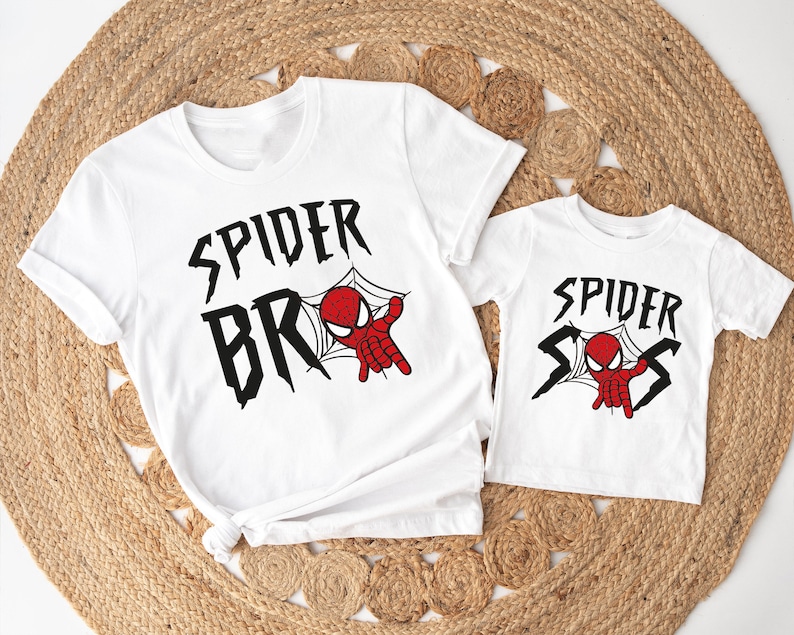 May include: Two white t-shirts with a Spider-Man design. The larger shirt says "Spider Bros" with a cartoon Spider-Man in a web. The smaller shirt says "Spider Sis" with a cartoon Spider-Man in a web.