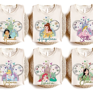 K&ouml;nnte beinhalten: Sechs wei&szlig;e T-Shirts mit einer Disney-Prinzessin und dem Text "Hannah", "Angelina", "Stella", "Victoria", "Aurora" und "Elena" bedruckt.