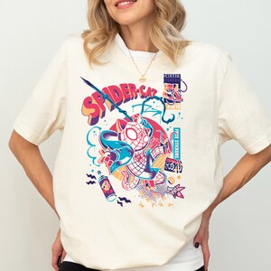 K&ouml;nnte beinhalten: Ein wei&szlig;es T-Shirt mit einem bunten Grafikdruck eines Katers, der ein Spiderman-Kost&uuml;m tr&auml;gt. Die Grafik enth&auml;lt den Text "SPIDER-CAT" und "FREE STICKERS".