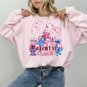 a woman wearing a pink sweatshirt with a castle on it