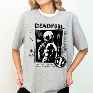 May include: A gray t-shirt with a black and white graphic print of Deadpool. The graphic includes the text "Deadpool", "Maximum Effort", and "They call me the merc with a mouth".