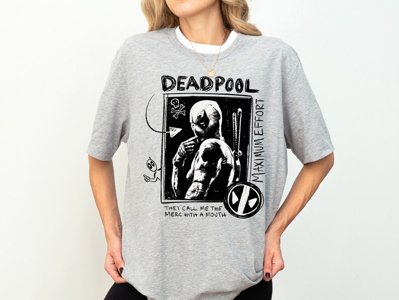 May include: A gray t-shirt with a black and white graphic print of Deadpool. The graphic includes the text "Deadpool", "Maximum Effort", and "They call me the merc with a mouth".
