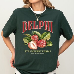 Puede incluir: Una camiseta verde oscuro con un gr&aacute;fico rojo y blanco de fresas y el texto "DELPHI STRAWBERRY FARMS - LONG ISLAND SOUND -"