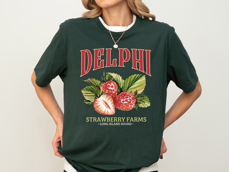 Puede incluir: Una camiseta verde oscuro con un gr&aacute;fico rojo y blanco de fresas y el texto "DELPHI STRAWBERRY FARMS - LONG ISLAND SOUND -"
