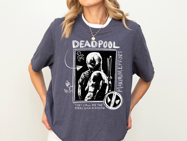 May include: A dark blue t-shirt with a white graphic of Deadpool, a comic book character. The graphic includes the text "Deadpool Maximum Effort" and "They call me the merc with a mouth".