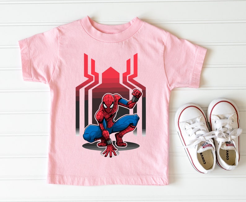 May include: Pink t-shirt with a cartoon image of Spiderman in a crouching pose. The image is set against a red and black web design.