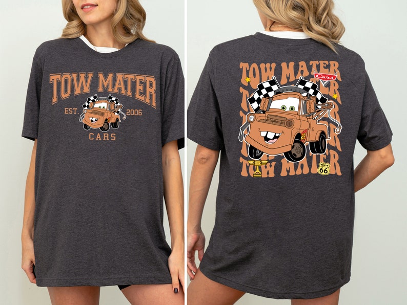 K&ouml;nnte beinhalten: Ein dunkelgraues T-Shirt mit einem Cartoon-Bild von Tow Mater aus dem Disney Pixar Film Cars. Die Vorderseite des Shirts zeigt "Tow Mater" mit "Est. 2006" und "Cars" darunter. Die R&uuml;ckseite des Shirts zeigt ein gr&ouml;&szlig;eres Bild von Tow Mater mit dem Text "Tow Mater" in einer Retro-Schrift.