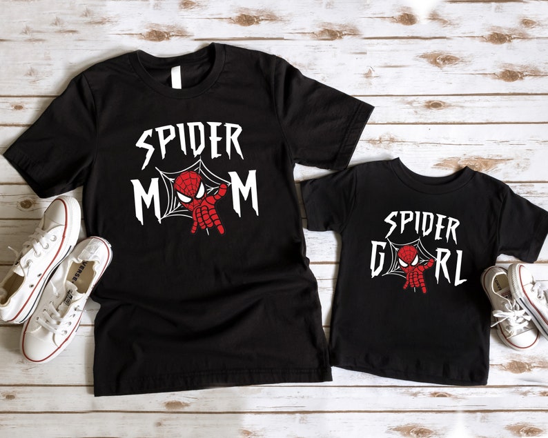May include: Two black t-shirts with a spider-man graphic. The larger shirt says "Spider Mom" and the smaller shirt says "Spider Girl".
