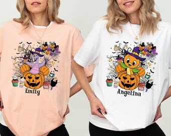 May include: A light peach t-shirt and a white t-shirt, each featuring a graphic of a character in a jack-o'-lantern with spiderwebs, bats, and sweets. The peach shirt has the name Emily, and the white shirt has the name Angelina printed below.