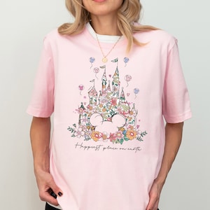 Pu&ograve; includere: Maglietta rosa con una stampa floreale del castello di Cenerentola e le parole "Happiest place on earth".