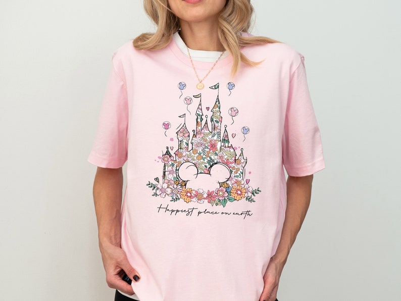 Pu&ograve; includere: Maglietta rosa con una stampa floreale del castello di Cenerentola e le parole "Happiest place on earth".