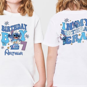 以下が含まれることがあります： 青と紫の文字と画像が描かれた白いTシャツ2枚。前のTシャツには「Birthday Boy」と青いスティッチのキャラクターと数字の7が書かれている。後ろのTシャツには「In My Birthday Era」と青いスティッチのキャラクターが書かれている。両方のTシャツには青と白のケーキの画像が描かれている。