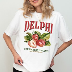 Puede incluir: Camiseta blanca con un estampado gr&aacute;fico rojo y verde de fresas y el texto "DELPHI STRAWBERRY FARMS - LONG ISLAND SOUND -"