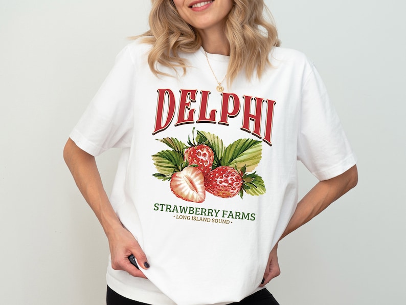 Puede incluir: Camiseta blanca con un estampado gr&aacute;fico rojo y verde de fresas y el texto "DELPHI STRAWBERRY FARMS - LONG ISLAND SOUND -"