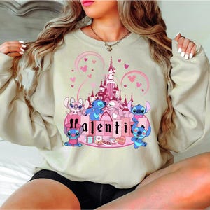 a woman sitting on a bed wearing a sweatshirt with a castle on it