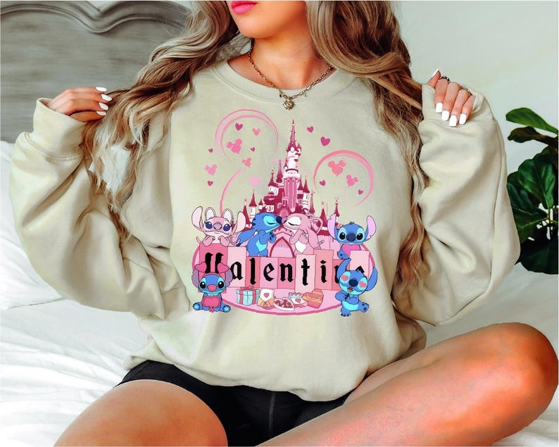 a woman sitting on a bed wearing a sweatshirt with a castle on it