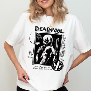 May include: White t-shirt with a black and white graphic print of Deadpool. The graphic features the text "Deadpool Maximum Effort" and "They call me the merc with a mouth".
