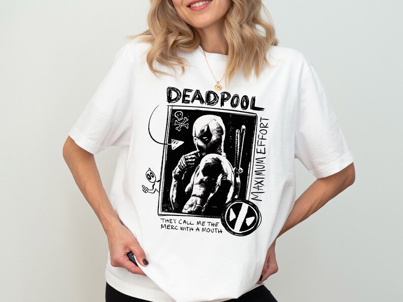 May include: White t-shirt with a black and white graphic print of Deadpool. The graphic features the text "Deadpool Maximum Effort" and "They call me the merc with a mouth".