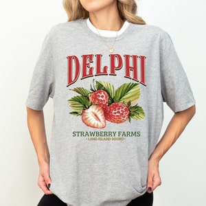Puede incluir: Camiseta gris con un gr&aacute;fico rojo que dice "DELPHI STRAWBERRY FARMS - LONG ISLAND SOUND -" con un dibujo de tres fresas.