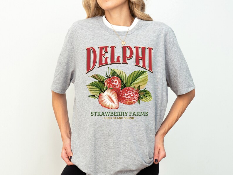 Puede incluir: Camiseta gris con un gr&aacute;fico rojo que dice "DELPHI STRAWBERRY FARMS - LONG ISLAND SOUND -" con un dibujo de tres fresas.