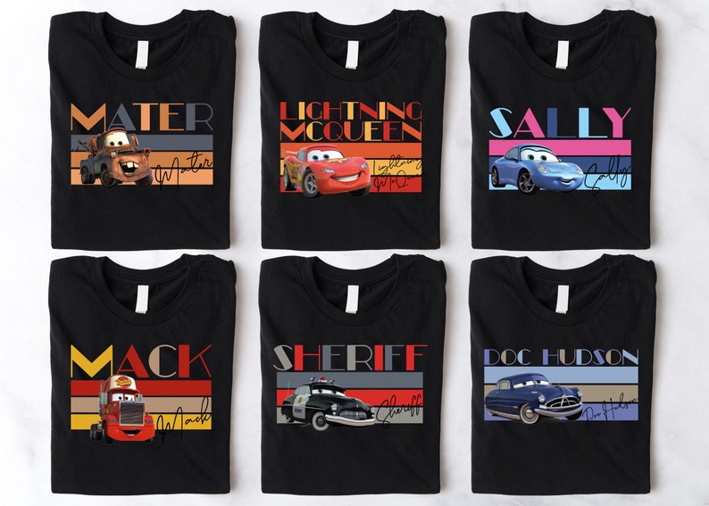 K&ouml;nnte beinhalten: Sechs schwarze T-Shirts mit bunten Retro-Grafiken, die Charaktere aus dem Disney Pixar Film Cars zeigen. Die Shirts zeigen Mater, Lightning McQueen, Sally, Mack, Sheriff und Doc Hudson.