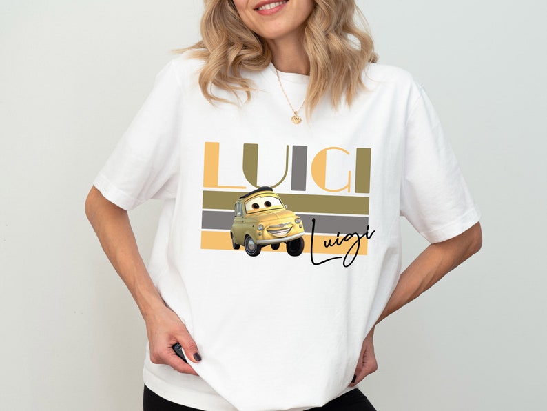 K&ouml;nnte beinhalten: Wei&szlig;es T-Shirt mit einem gelben Comic-Auto und dem Text "Luigi" in braunen, grauen und gelben Streifen.