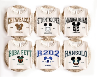 May include: Six off-white t-shirts featuring Star Wars character graphics in a collegiate font. Each shirt displays a character name, a Mickey Mouse-shaped icon with a character helmet or face, the text EST. 1977, and the Star Wars logo.