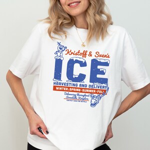 K&ouml;nnte beinhalten: Wei&szlig;es T-Shirt mit einem blauen und roten Grafikdruck mit dem Text "Kristoff & Sven's ICE HARVESTING AND DELIVERY WINTER SPRING-SUMMER-FALL Delivering throughout Arendelle Kingdom CONTACT SVEN FOR DETAILS" und Illustrationen von Olaf und Sven.