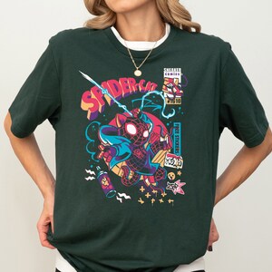K&ouml;nnte beinhalten: Ein dunkelgr&uuml;nes T-Shirt mit einem Grafikdruck eines Comic-Spider-Man-Charakters in einem rot-schwarzen Anzug. Die Grafik enth&auml;lt auch den Text "SPIDER-CAT" und "FREE STICKERS".
