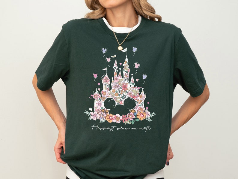 Pu&ograve; includere: Una maglietta verde scuro con una stampa floreale del castello di Cenerentola e il testo "Happiest place on earth".