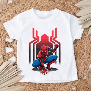 May include: White t-shirt with a red and blue Spiderman graphic. The graphic shows Spiderman crouching with his arms outstretched. The background is a black and red web design.