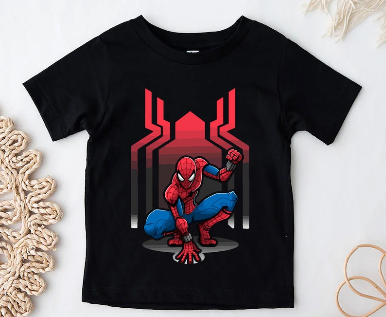 May include: Black t-shirt with a red and blue Spider-Man graphic. The graphic shows Spider-Man in a crouching pose with a red and blue suit and a red spider symbol on his chest. The background of the graphic is a red and black web design.