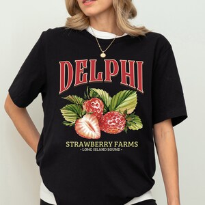 Puede incluir: Camiseta negra con un gr&aacute;fico rojo de fresas y el texto "DELPHI STRAWBERRY FARMS - LONG ISLAND SOUND -"