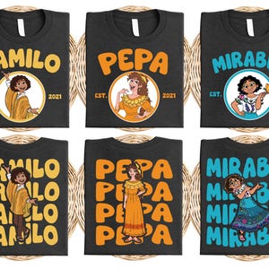 May include: Dark gray t-shirts featuring characters Camilo, Pepa, and Mirabel from a movie. Each shirt has a character's name in large letters, a character illustration, and the text "EST. 2021".