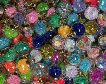 May include: A collection of small, clear glass ornaments filled with colorful glitter and confetti. The ornaments have gold-colored metal caps and loops for hanging. The glitter inside is various colors, including pink, green, blue, and yellow.