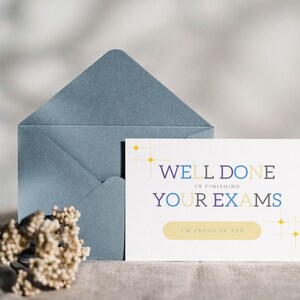 Puede incluir: Una tarjeta blanca con el texto "Well Done in finishing your exams" en letras de colores. La tarjeta tiene un botón amarillo que dice "I'm proud of you". La tarjeta está sobre una superficie marrón claro con un sobre azul detrás.