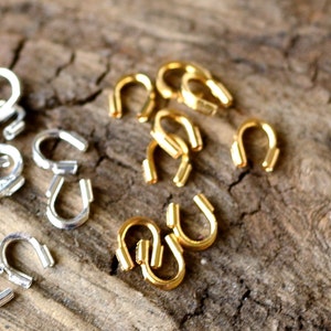 May include: A close-up of two groups of metal jump rings. One group is silver and the other is gold. The rings are arranged in a random pattern on a wooden surface.