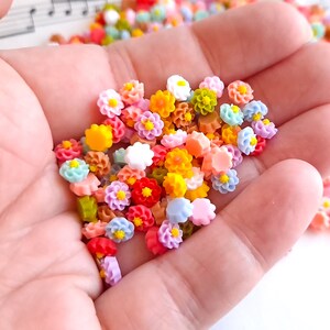 May include: A collection of colorful flower-shaped resin charms in various pastel colors, including pink, blue, yellow, and green. The charms are small and perfect for adding a touch of whimsy to crafts and jewelry.
