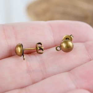 May include: Two gold-toned earring findings with a round ball at the top and a loop on the bottom. The findings are designed to be used with a variety of earring styles.