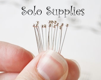 May include: A close-up of a hand holding a bunch of silver head pins with round heads. The pins are arranged in a fan shape. The text "Solo Supplies" is visible at the top of the image.
