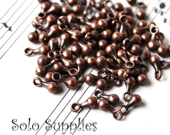 May include: A pile of copper-colored teardrop-shaped bead caps with a loop on each end. The bead caps are arranged on a sheet of music.