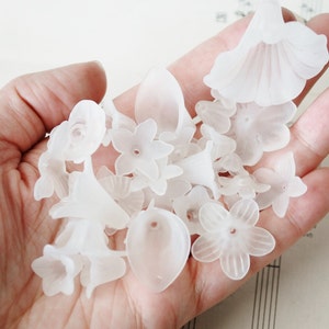 May include: A collection of white plastic flower-shaped beads. The beads are translucent and have a delicate, feminine appearance.