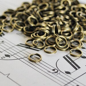 以下が含まれることがあります： 楽譜の上に置かれた、金色の金属製のジャンプリングの山。ジャンプリングは小さく丸く、ランダムなパターンで配置されています。