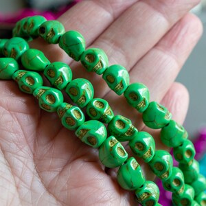 May include: Three strands of green skull beads. The beads are made of a smooth, green material with gold accents. The beads are strung on a clear string.