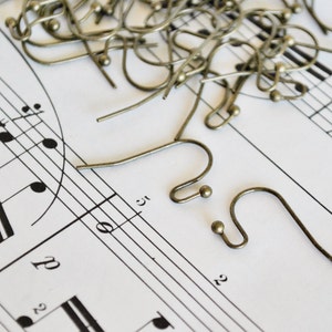 May include: A close-up of a pile of gold-toned earring hooks on a sheet of music. The hooks are made of metal and have a simple, classic design.