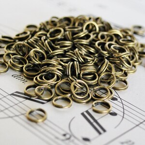 以下が含まれることがあります： 金色の金属製のジャンプリングがたくさん積まれています。リングはすべて同じサイズで、ランダムなパターンで配置されています。