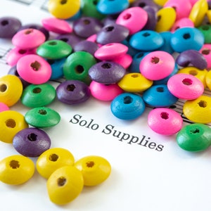 May include: A collection of colorful wooden beads in various shades of pink, blue, green, yellow, and purple. The beads are scattered on a white surface with the text "Solo Supplies" printed on it.