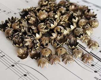May include: A large pile of gold-colored metal flower-shaped bead caps. The bead caps are scattered on a white sheet of music.