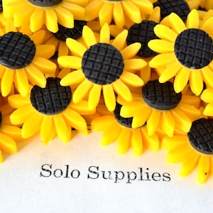 May include: A close-up of yellow sunflower-shaped embellishments with black centers. The petals are bright yellow, and the centers are textured. The text "Solo Supplies" is printed in black at the bottom.